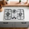 "Stainless steel kitchen stove with three burners and control knobs, illuminated by overhead lighting,