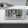 RINO RS979 Gas Stove (Brass),"Stainless steel kitchen stove with three burners and control knobs, illuminated by overhead lighting,