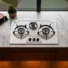 Gas Stove,"Stainless steel kitchen stove with three burners and control knobs, illuminated by overhead lighting,